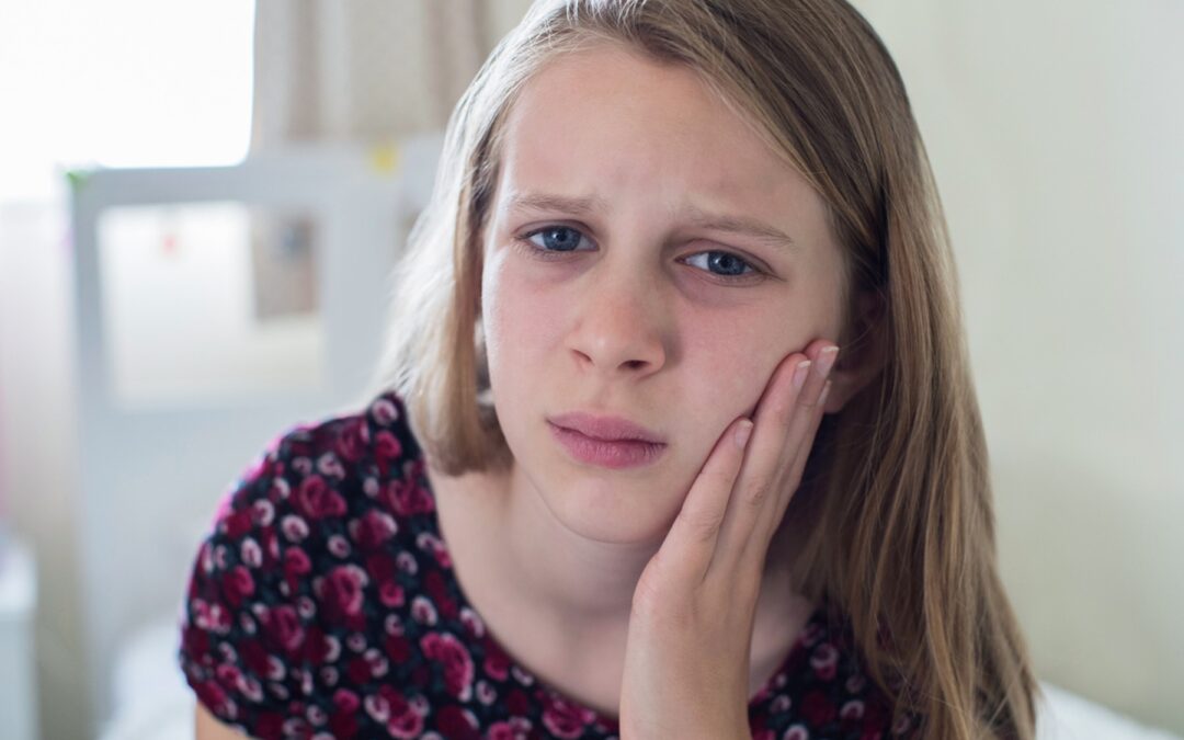 A child with her hand on her cheek, Children's Tooth Pain: When to See a Specialist