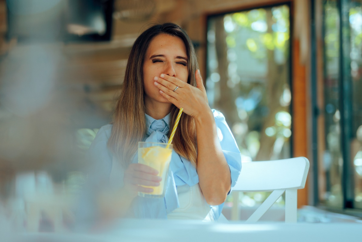 Adult reacting to tooth sensitivity while drinking a cold beverage.