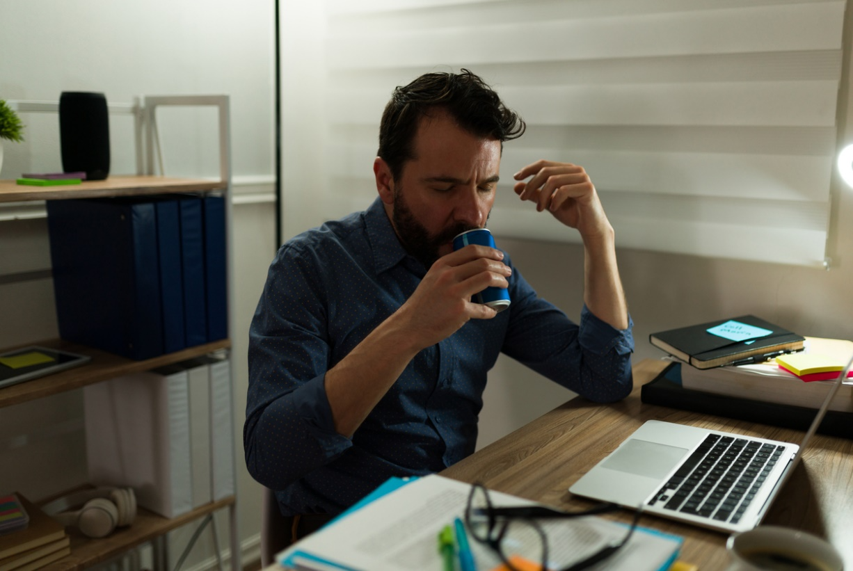 Adult drinking an energy beverage while working late at a computer to illustrate energy drinks and tooth damage.