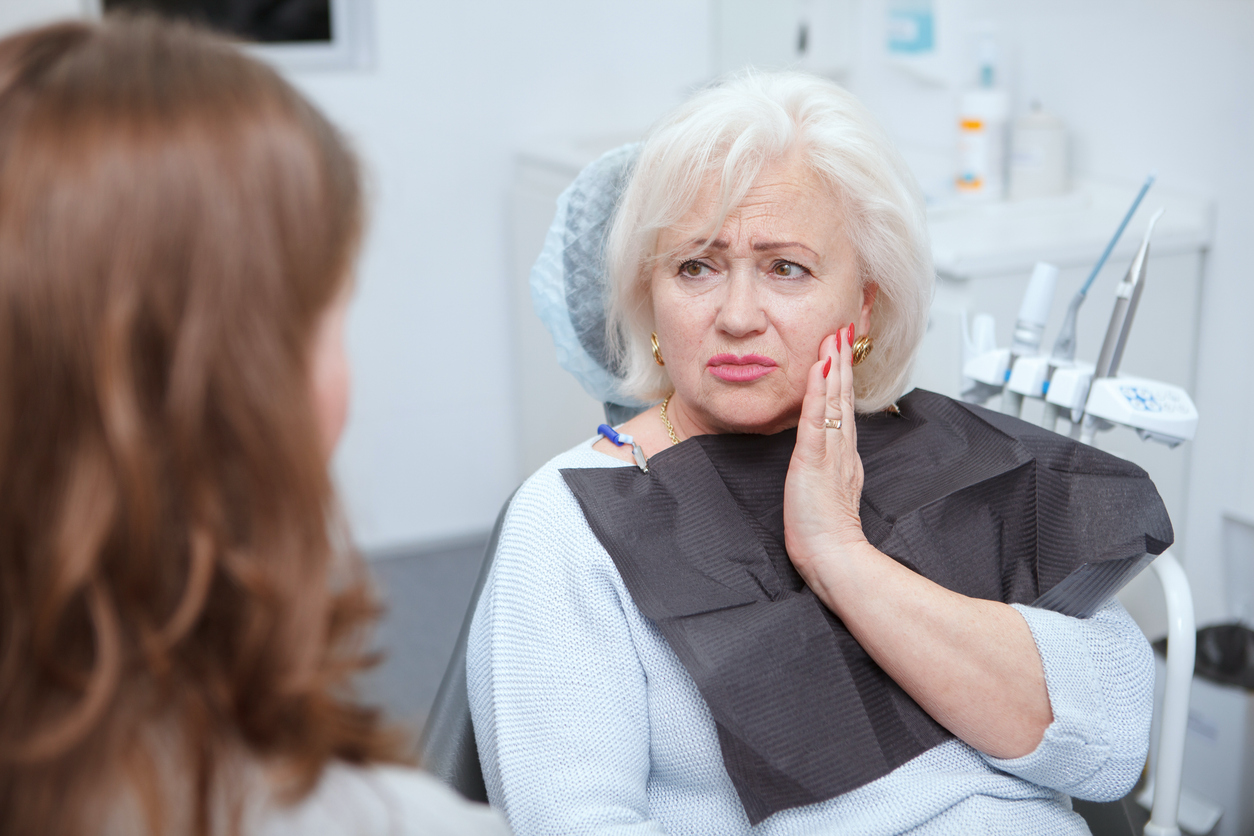 Patient holding her cheek while discussing tooth pain with a dental professional.